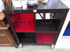 A black ask finished storage unit with dark red plastic drawers.