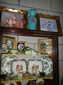 Three shelves of ceramics and two gilt framed pictures.