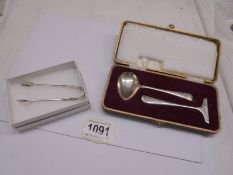 A cased silver spoon with pusher and a pair of silver sugar tongs.