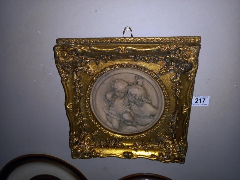 An ornate gilt framed plaque of children, diameter 17cm, frame 29cm x 29cm