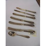 Six silver handled butter knives and a silver spoon.