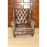 Deep buttoned leathere upholstered armchair on brass castors {96 cm H x 94 cm W x 70 cm D}.
