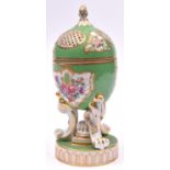 A Egg-shaped porcelain pomander, with floral decorations on a green base. Hinged lid with pierced