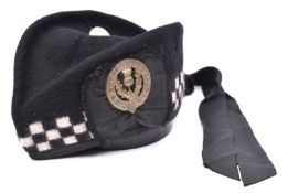 A Scottish glengarry cap, with black and white diced band, two tails, and replica brass badge of the