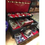 A black jewellery box containing various items of costume jewellery including yellow metal and