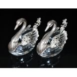 A pair of novelty white metal mounted glass salts, each modelled as a swan, with spoons, length 7cm.