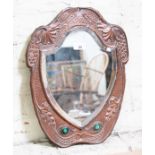 An Arts & Crafts copper mirror, shield shape and set with green cabochons, 35.5cm x 45cm.