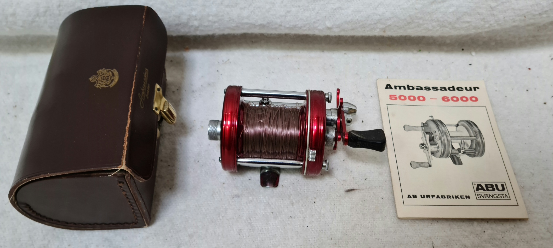 An Abu Ambassadeur 6000 fishing reel in leather carrying case with handbook