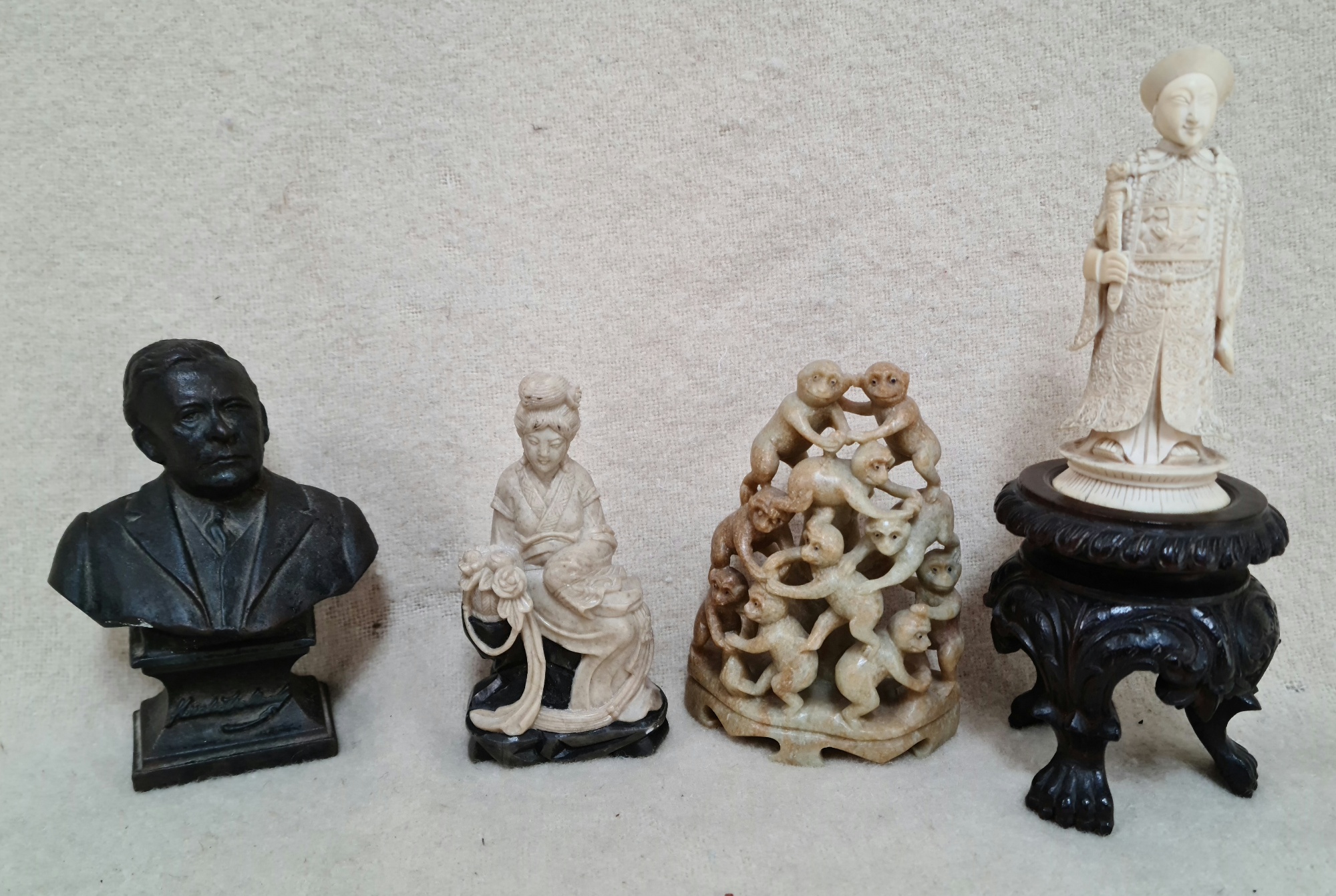 A carved ivory figure on carved wood stand, 2 soapstone Oriental group figures and a cast metal