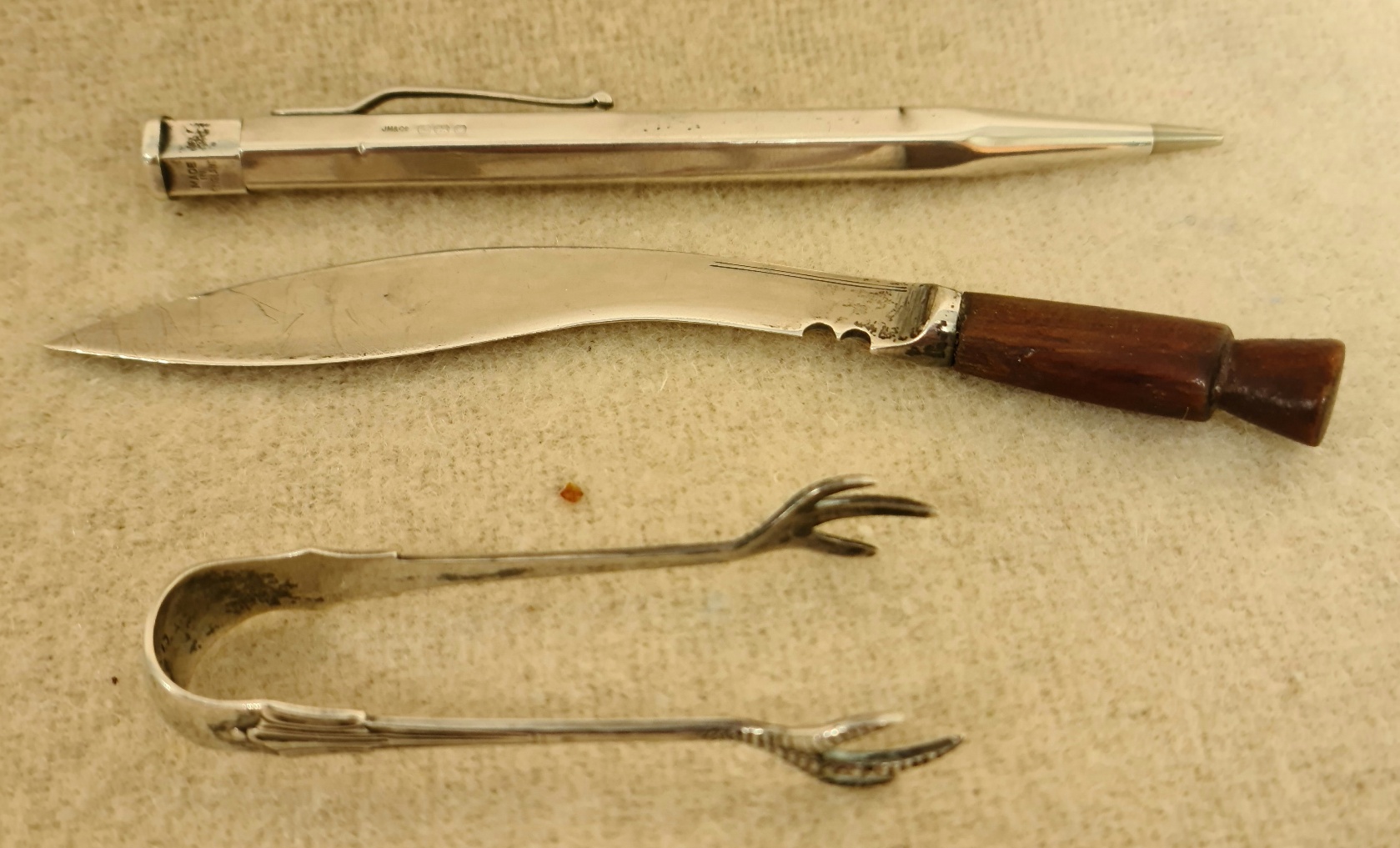 Hallmarked silver comprising a silver bladed kukri knife, a pair of sugar tongs and a propelling