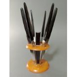 An Art Deco black and butterscotch bakelite knife stand of circular form with six knives, the