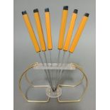 A vintage wire frame knife stand with six butterscotch and black bakelite knives, the steel blades