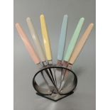 An Art Deco curved black plastic stand with six multi-coloured handled knives, the steel blades