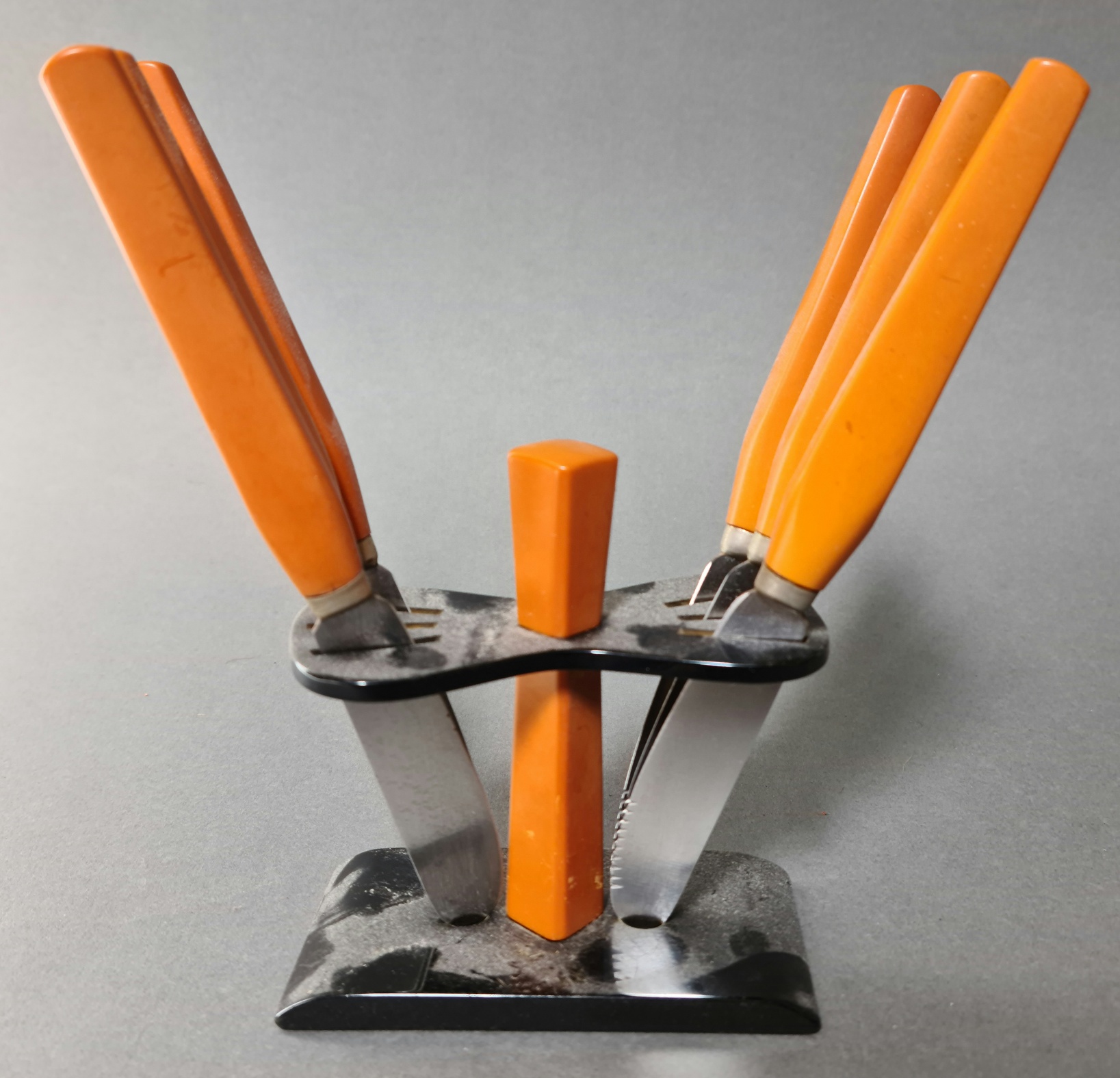 An Art Deco bakelite knife stand with a set of six orange bakelite handled knives, the serrated