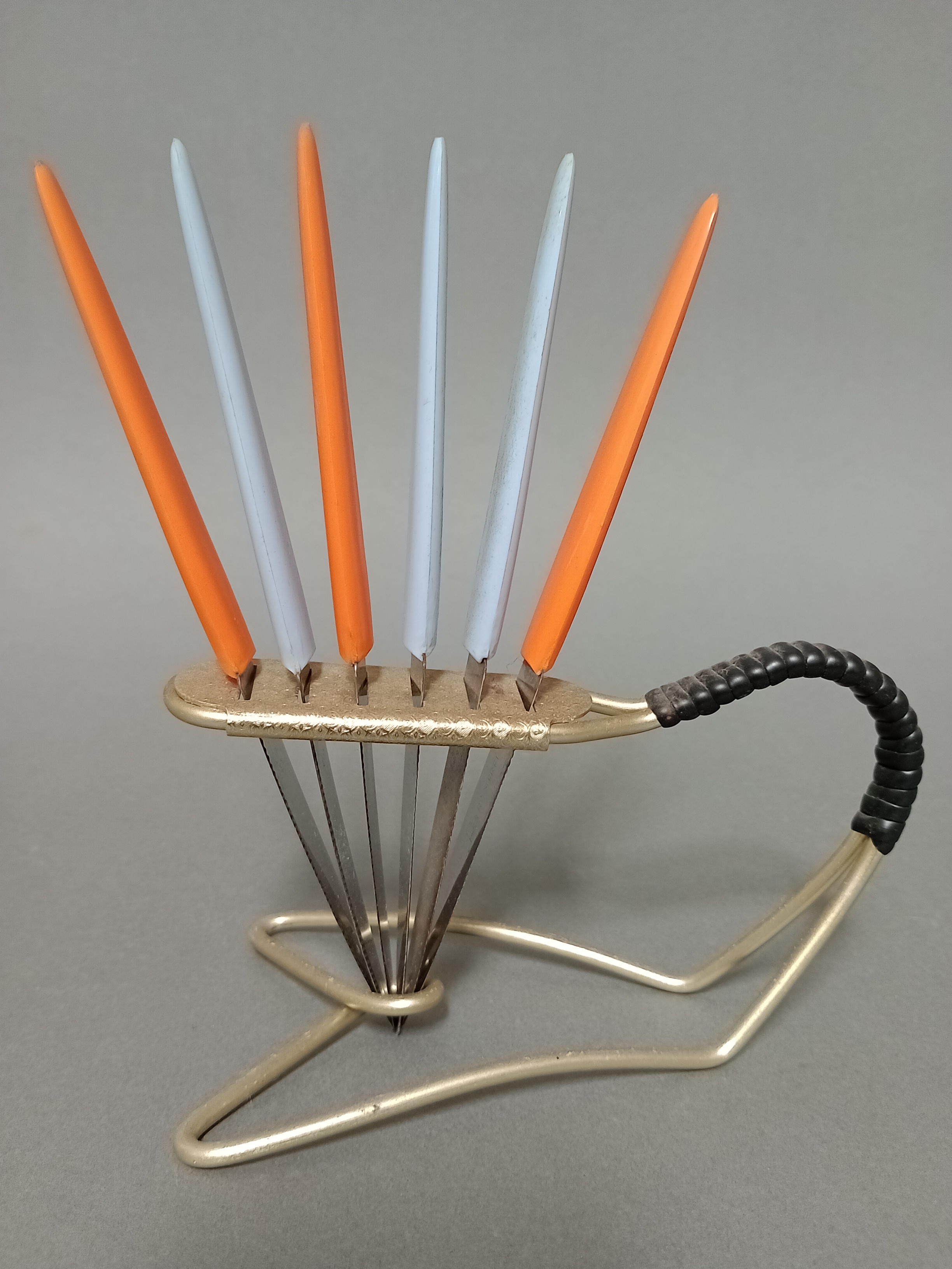 A vintage gilt metal knife stand with rubber bound handle and six multi-coloured plastic handled