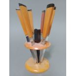 An Art Deco black and butterscotch bakelite knife stand of circular form with six knives, the