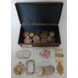 An antique decorated metal box with contents to include coins, badges, etc.