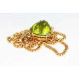 A peridot pendant, the triangular cut stone weighing approx. 7ct, mounted in 9ct gold and hung on