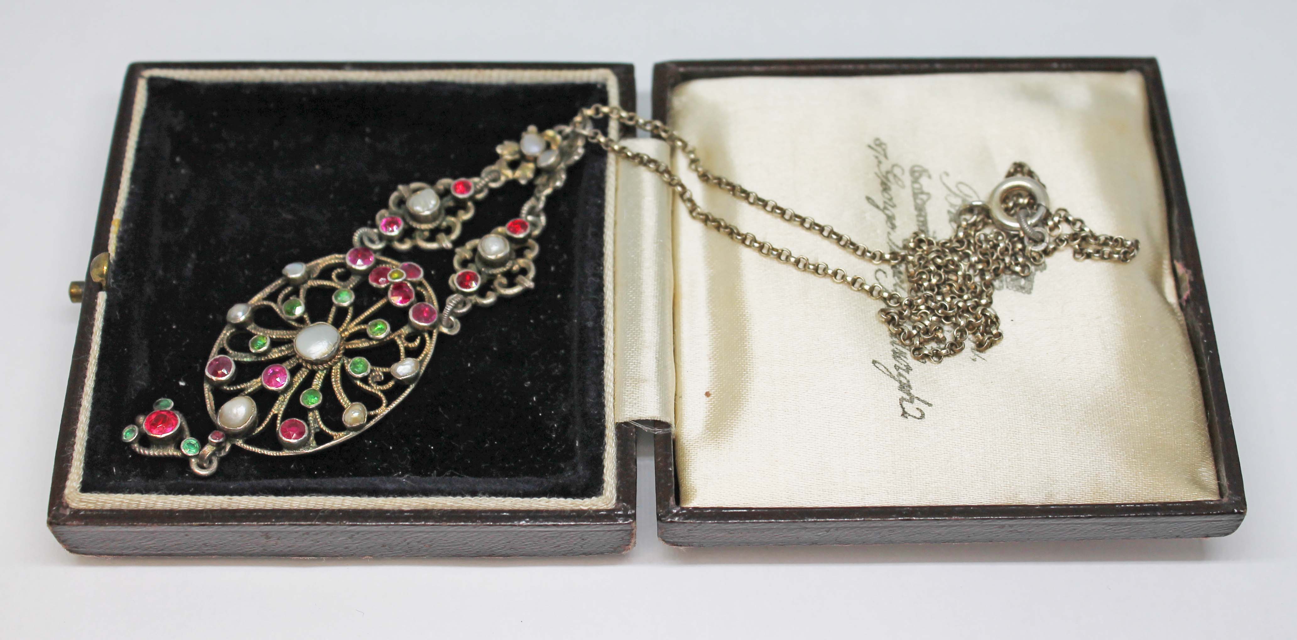 A filigree pendant set with rubies, paste, pearls and green stones, white metal, unmarked, chain
