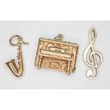 A group of three hallmarked 9ct gold musical themed charms comprising a piano, a saxophone and a