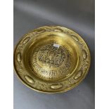 A large repoussé brass charger "alms dish" with raised centre depicting two men transporting a large