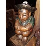 A painted carved wood figure of a boy, seated.