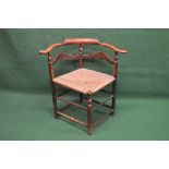 Early 19th century elm corner chair having scrolled arms and shaped back rails, the rush seat