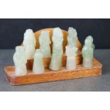 A group of ten carved jade oriental figures on wooden stand.