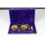 A set of brass scales and weights within a purple velvet storage box.