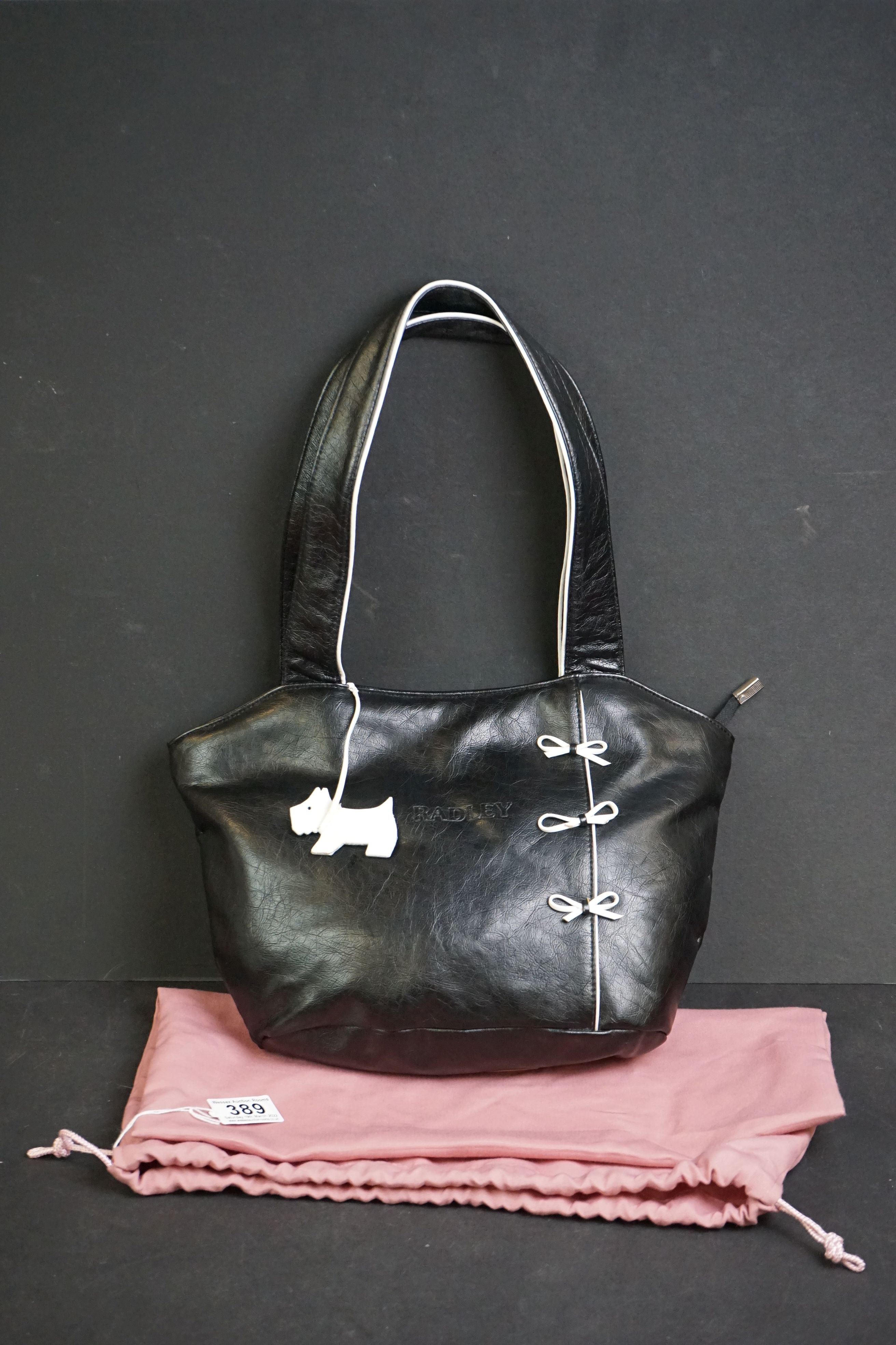 A black Radley handbag with white bow detailing, white Radley dog and pink dust bag.