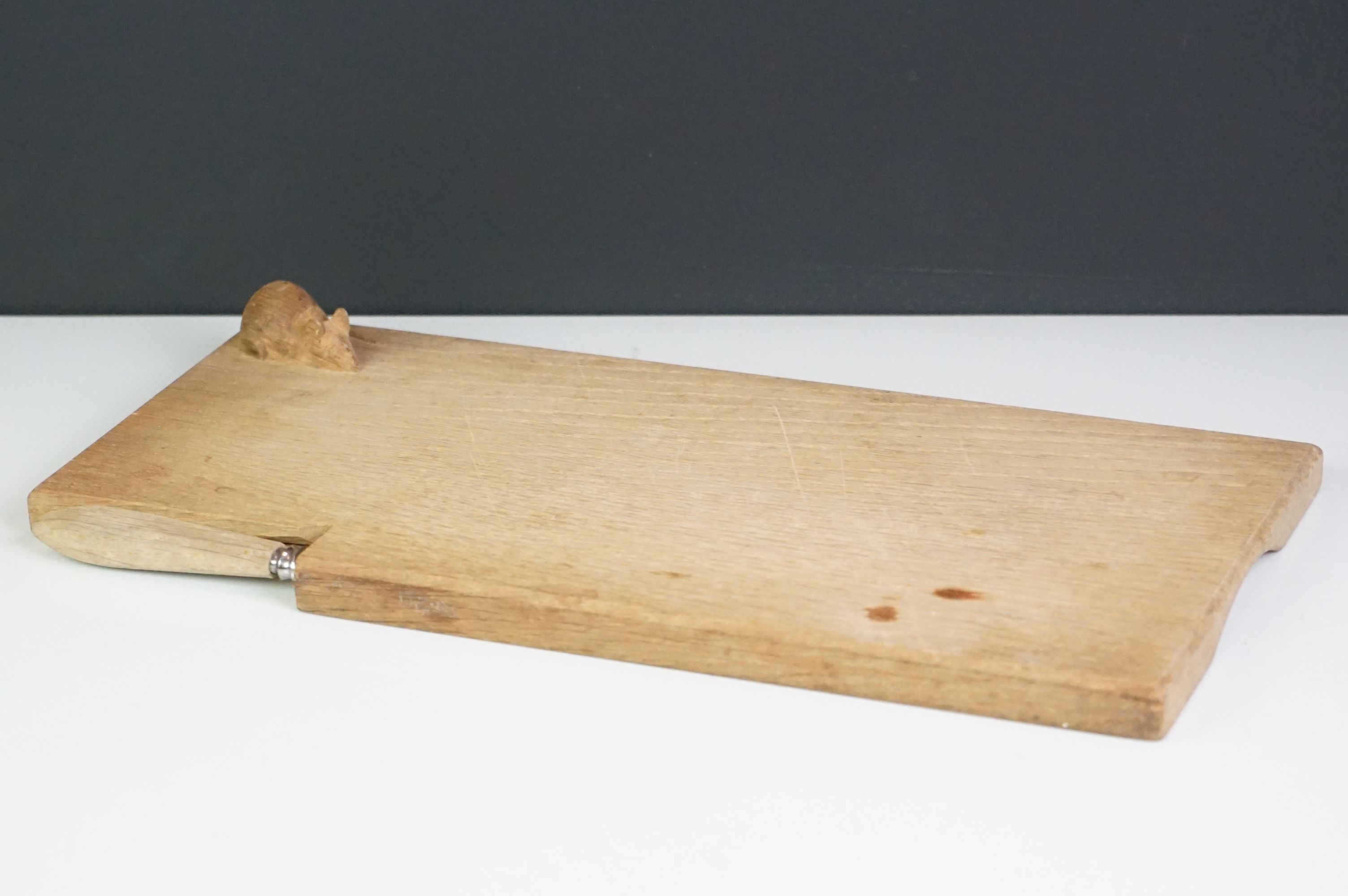 A wooden cheese board and cheese knife in the style of Mouseman Robert Thompson.