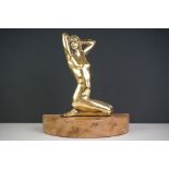 An Art Deco brass figure of a nude female kneeling on a wooden plinth.