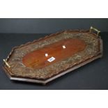 A wooden serving tray with brass handles and hand carved floral decoration.