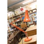 A orange angle poise lamp together with a wooden table lamp.