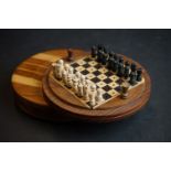 A wooden pocket chess set contained within a turned wooden case.