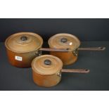 A set of three copper graduated saucepans with iron handles.