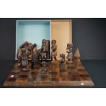 A hand carved wooden tribal chess set together with board.