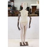 Female Shop Mannequin with cloth covered head and body, wooden articulated arms and plastic legs,