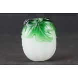 Small glass bottle carved in the form of a fruit sat amongst leaves, with green leaf overlay on whi
