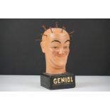 Grotesque plaster bust of a man with nails in skull raised on a plinth marked ' Geniol ', approx