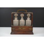 Late Victorian oak tantalus with brass Gothic style mounts, containing three hobnail cut glass