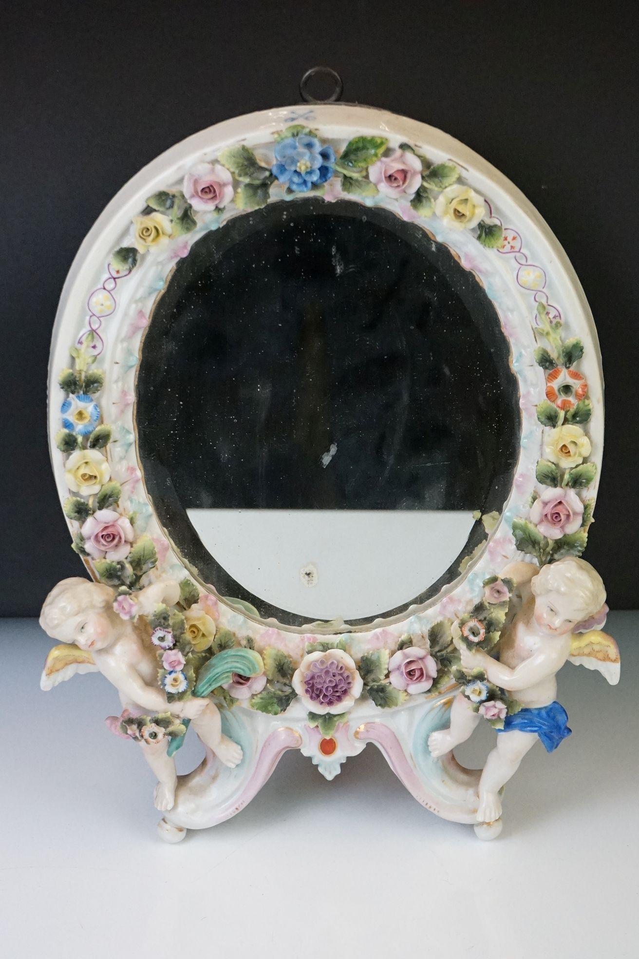 Dresden porcelain dressing table mirror of oval form, with bevel glass surmounted by two cherubs