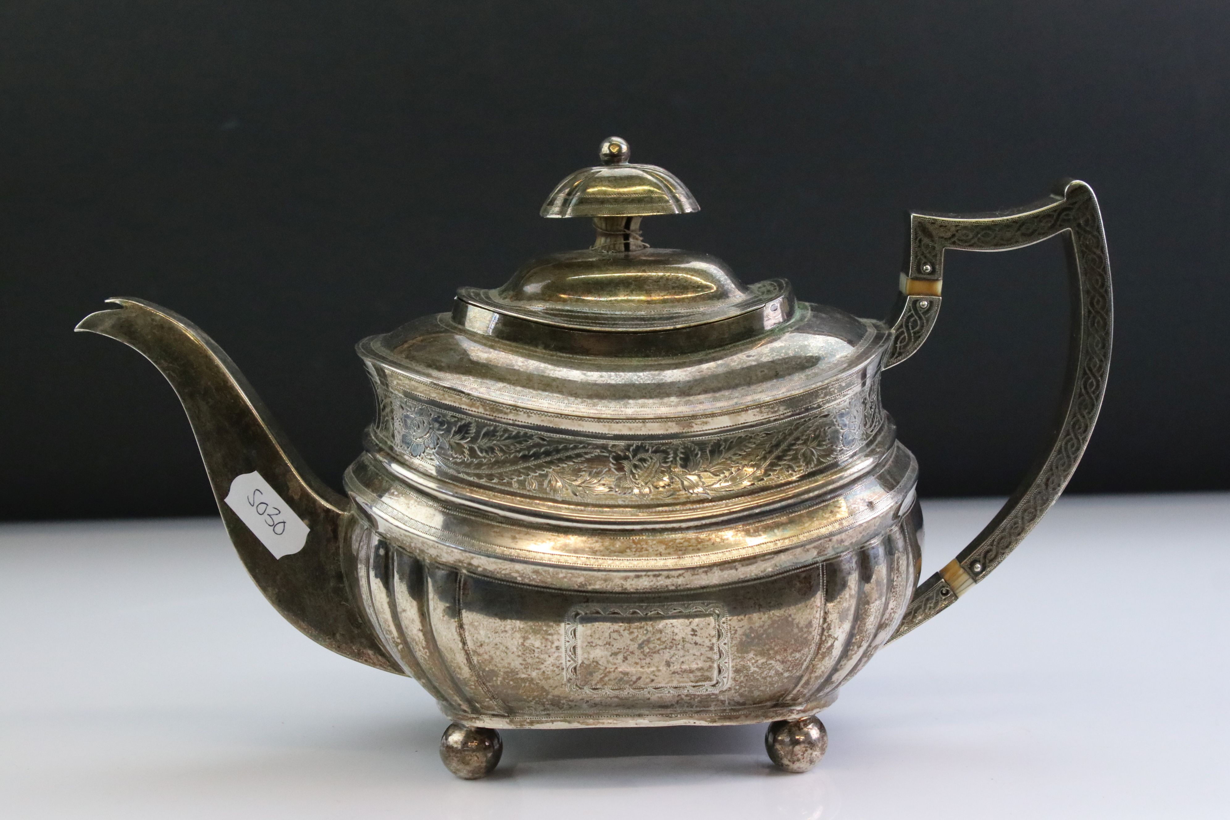 George III silver teapot raised on four ball feet, engraved floral and foliate decoration to the