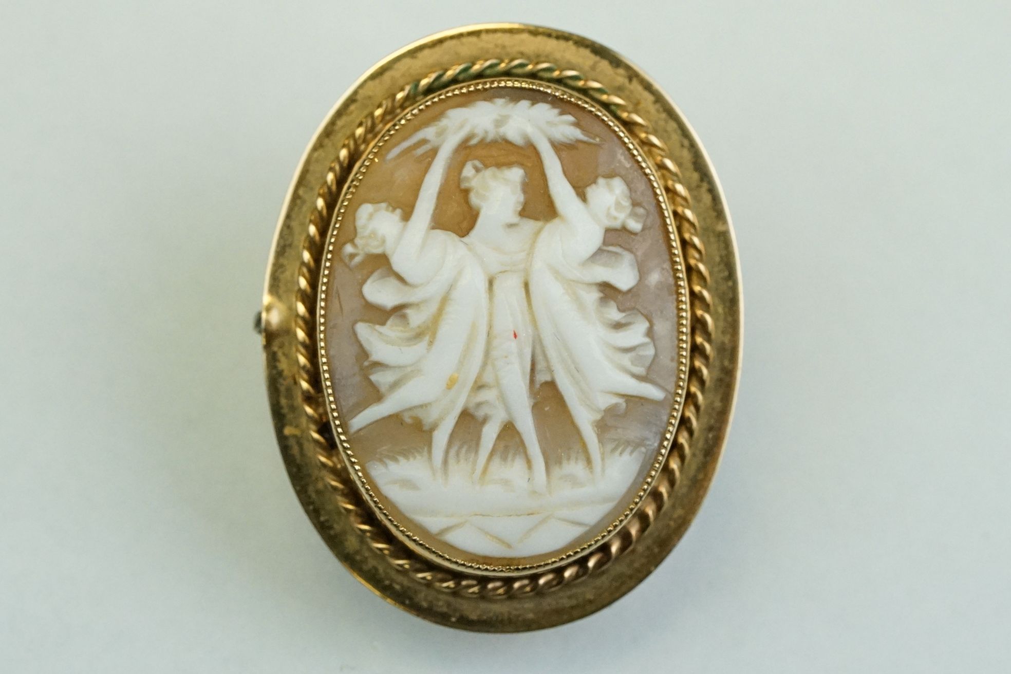 Shell cameo 9ct yellow gold brooch, the oval cameo depicting the Three Graces, rubover set with