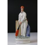 19th Century Staffordshire figure of a batsman wearing an orange cap, a cream spotted shirt, holding