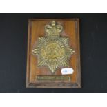 A brass Metropolitan police New Scotland Yard badge on wooden wall plaque.