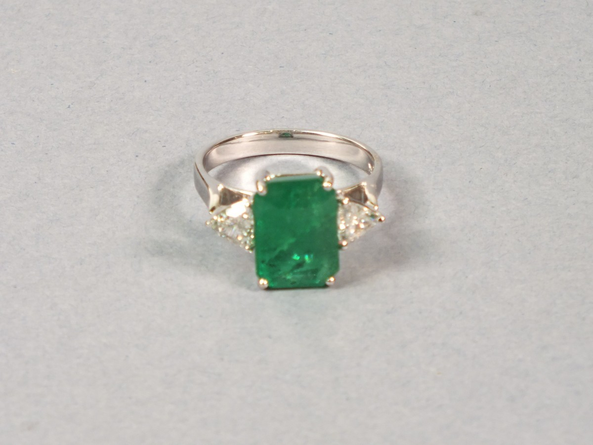 An emerald and diamond dress ring, set in 18ct white gold, the emerald cut central stone flanked