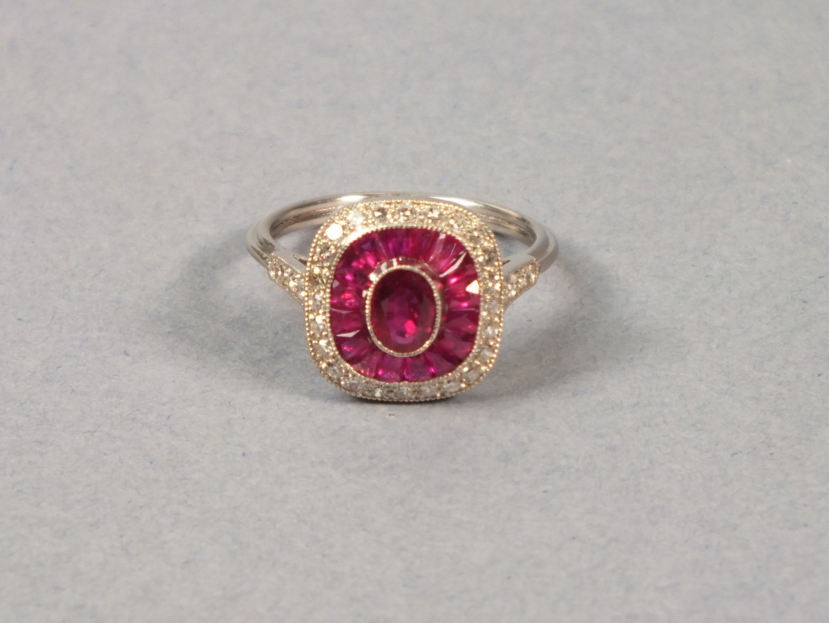 A platinum ruby and diamond dress ring, the central stone within a band of calibre cut rubies with a