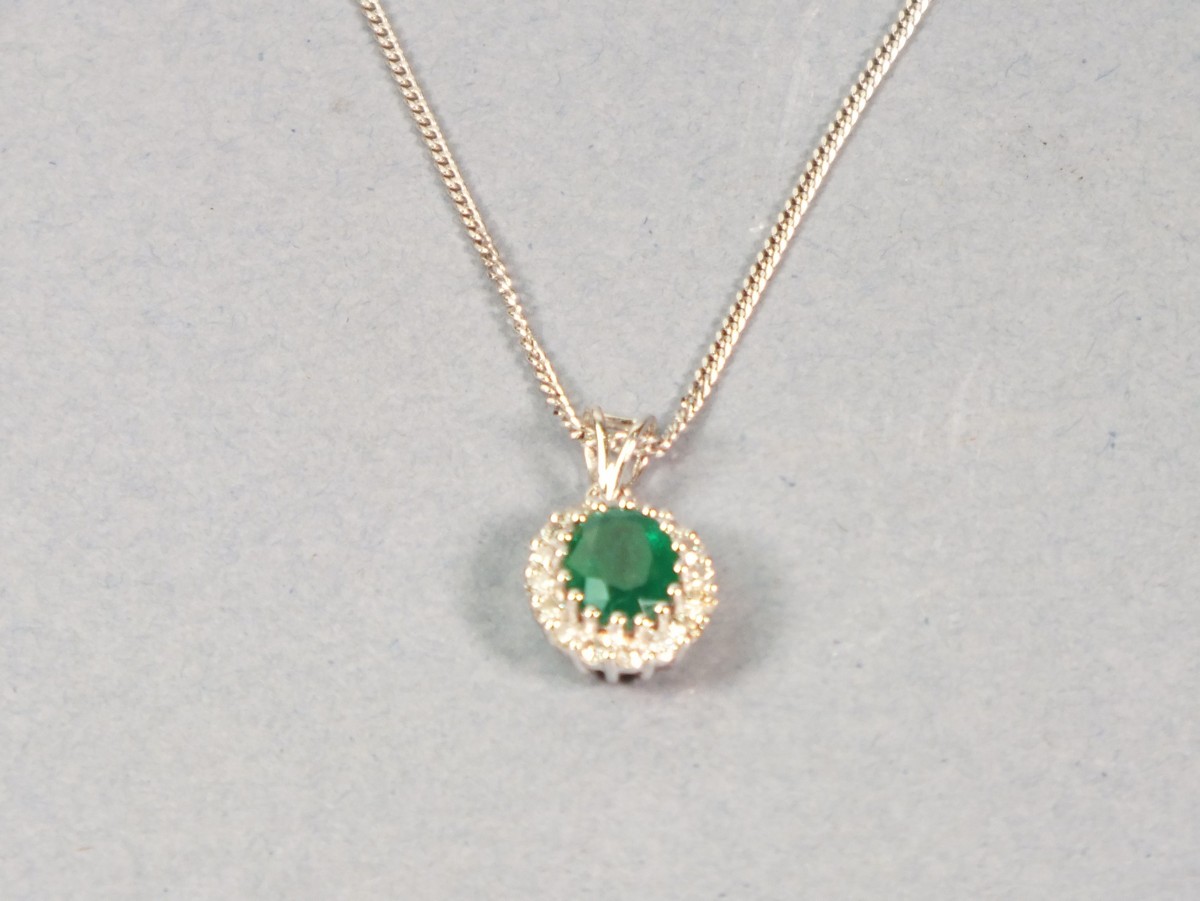 A diamond and emerald pendant, the oval cut central stone within a band of diamond, set in 18ct