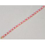 An 18ct gold ruby and diamond line bracelet, the arrangement of oval cut stones interspersed with